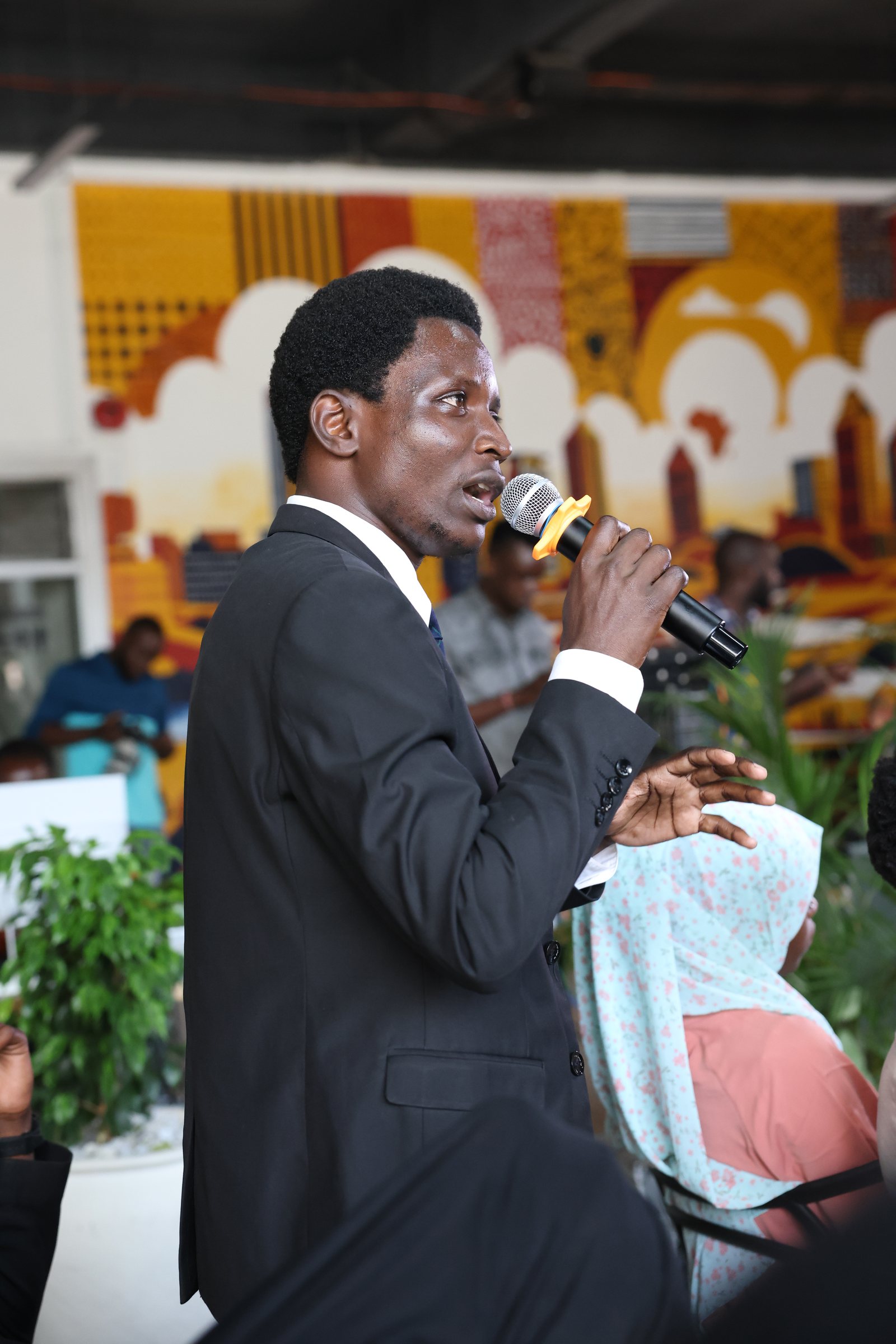 A young man in a suit speaking into a microphone from the floor